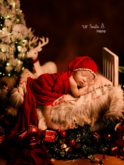 A tiny Santa dreaming of Christmas. This beautiful shot captures a newborn sleeping peacefully in a miniature bed surrounded by festive decorations.