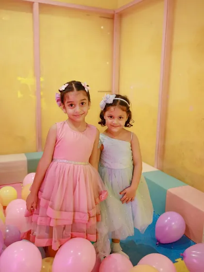 Two little princesses enjoying a magical birthday party, complete with beautiful dresses and a balloon-filled play area.