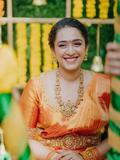 A bride smiling during her Haldi ceremony. She wears a beautiful orange tie-dye saree with a custom blouse featuring delicate embroidery.