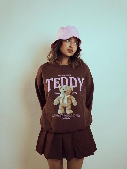 A playful and cute studio shot of influencer Diksha Rawat. The teddy bear sweatshirt and bucket hat create a fun, youthful look that showcases her personality.