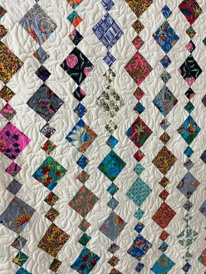 A close-up of the Chandelier quilt, showing the variety of fabrics and the feather-like quilting in the background.