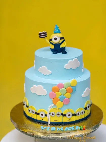 A showstopper cake for a Minions-themed birthday. This two-tiered cake is decorated with clouds, balloons, and a Minion topper, perfectly capturing the fun of the theme.