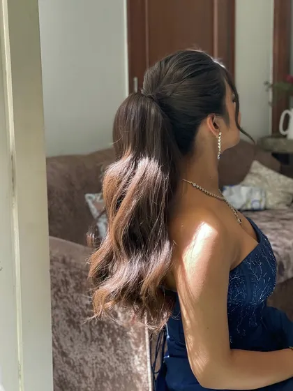 A side view of a voluminous ponytail with soft waves. I create a wrap around base using the hair itself for a seamless and polished finish.