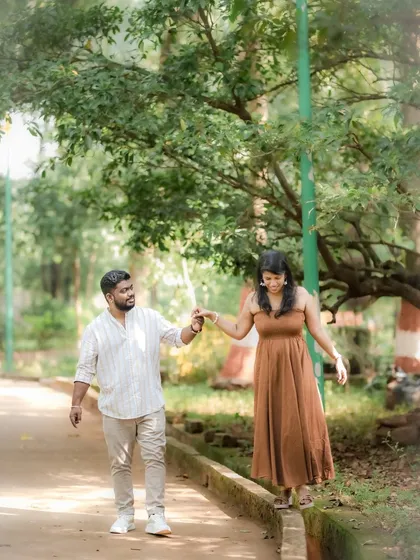 A playful and candid shot of a couple walking in a park, with the bride balancing on a ledge while holding her partner's hand. This captures their fun-loving dynamic.