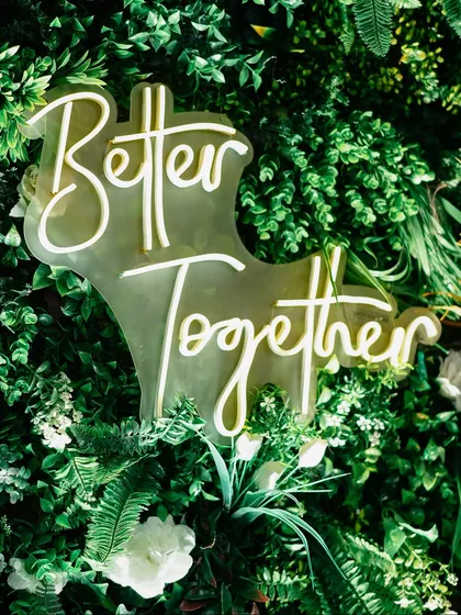 A custom neon sign saying "Better Together" nestled in a lush green floral wall. It's these personalized details that make a wedding feel unique.