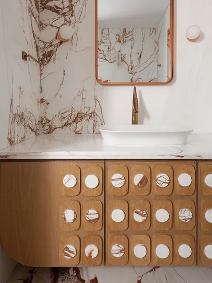 A powder room that makes a statement with dramatic red-veined white marble wrapping the walls and floor. We designed a custom wood veneer vanity with unique marble-inlaid circular details on the drawers.
