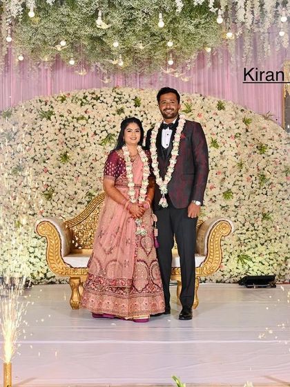 This reception stage features a massive cascade of white flowers, creating a luxurious and textured backdrop. The cold sparklers add a celebratory sparkle to the couple's portrait.