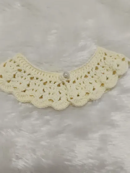 This delicate cream-colored collar features a lacy, openwork pattern and a single pearl button. It’s a vintage-inspired design that adds elegance to any little outfit.