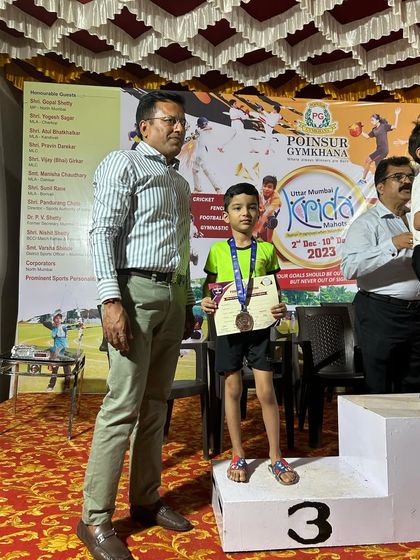 A student stands on the third-place podium at the Poisor Gymkhana Gymnastics Competition. It's a proud moment for him and a testament to the hard work of his coaches.