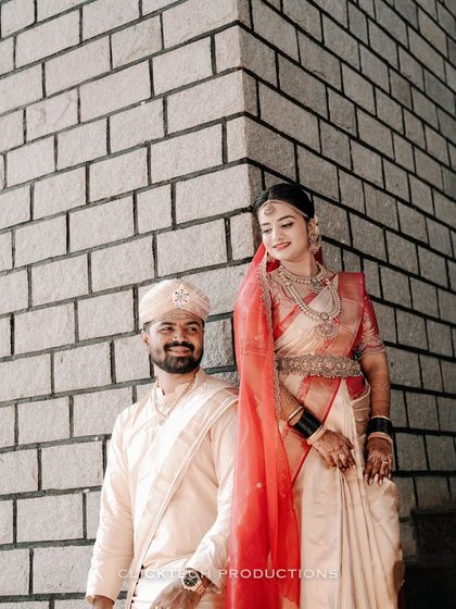 A stylish portrait of a South Indian couple in their wedding attire, posing against a modern brick wall, showcasing a blend of traditional and contemporary aesthetics.