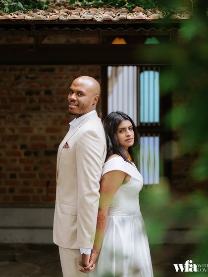 A modern pose against a classic backdrop. The couple stands back-to-back, creating a stylish portrait against the brick walls and stained-glass windows.