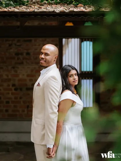 A modern pose against a classic backdrop. The couple stands back-to-back, creating a stylish portrait against the brick walls and stained-glass windows.