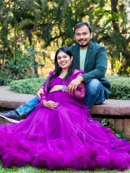 A comfortable and happy portrait of a couple sitting together in a park, with the mom-to-be's vibrant purple gown spread out beautifully.