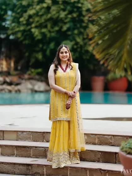 A full-length shot of the bride in her vibrant yellow mehndi outfit. She stands confidently by the pool, ready for the fun-filled celebrations.