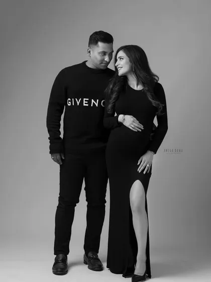 A stylish full-length portrait in black and white. The couple's coordinated designer outfits and confident poses create a modern and chic maternity photo.