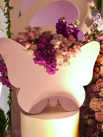 A custom-made butterfly-shaped planter filled with purple and pink flowers, serving as a unique decor piece on a white pedestal.
