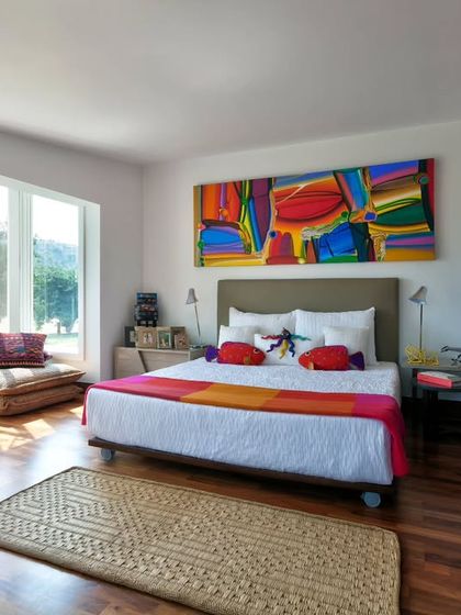 A vibrant bedroom at Aishbagh, where a colourful abstract painting and bright textiles bring energy to the space. Low seating by the window creates a casual nook for enjoying the natural light and views of the surrounding landscape.