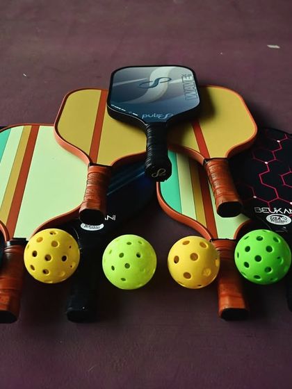 I've got all the gear you need. A colorful lineup of pickleball paddles and balls ready for action, showcasing the quality equipment available for players at my academy.