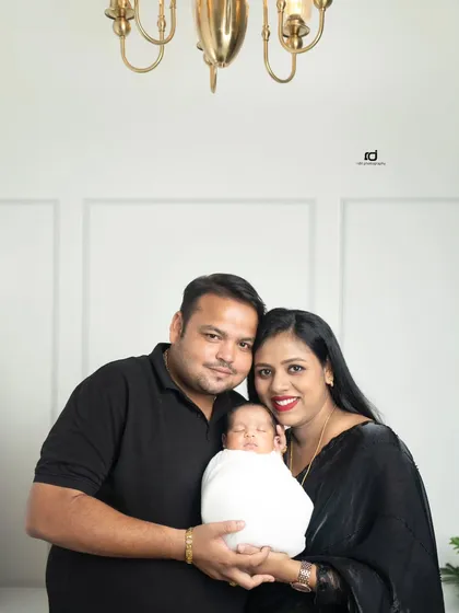 A beautiful, formal portrait of the new family. Dressed in black against a bright white background, the focus is entirely on their happy faces and their precious newborn.