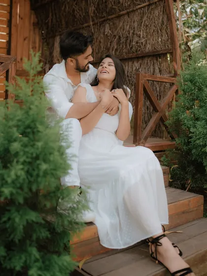 A joyful, candid moment on the steps of a rustic cabin. The couple's coordinated white outfits and genuine laughter make this a heartwarming and authentic pre-wedding photograph.
