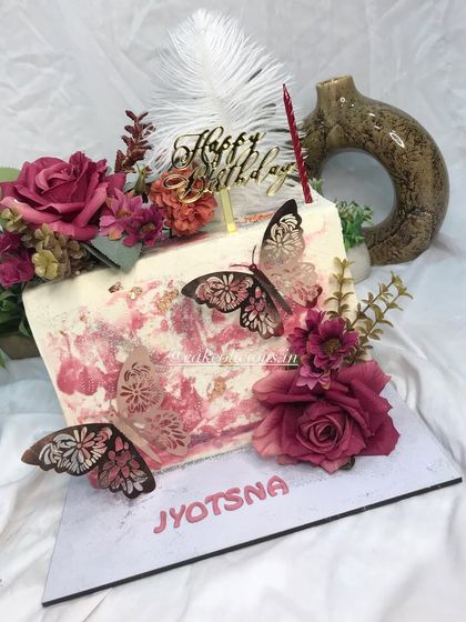My first rectangular top-forward cake, and it came out so perfectly. This floral beauty features a white chocolate ganache with a pink textured effect, adorned with deep red roses, elegant butterflies, and a feather. The flavor inside is classic pineapple.