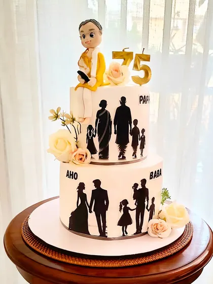 A grand two-tier cake celebrating a 75th birthday, decorated with family silhouettes that tell the story of a growing family. A custom fondant figure sits on top, representing the patriarch.