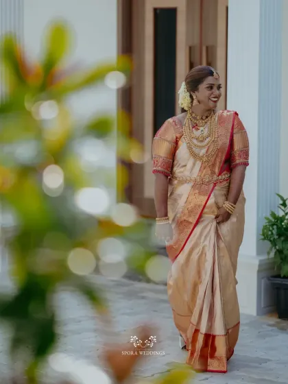 A joyful, candid shot of the bride in her beautiful silk saree, her smile lighting up the frame as she walks through the venue.