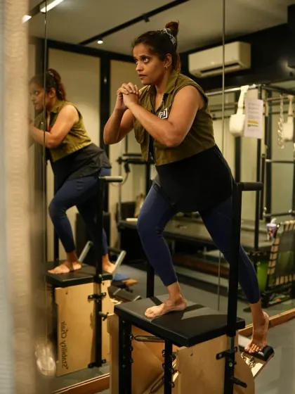 The reflection in the mirror shows the focus and precision required for this lunge variation on the Pilates chair. This exercise challenges the entire lower body and core, essential for building a strong athletic foundation.