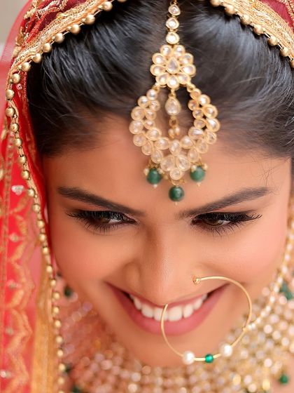 A beautiful close-up of a smiling bride looking down, showcasing her intricate maang tikka and bridal jewelry. This detailed shot is a perfect example of our focus on bridal portraits.
