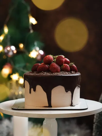 A moody shot of a chocolate strawberry drip cake with a festive Christmas tree bokeh in the background. This image is perfect for holiday marketing and social media.