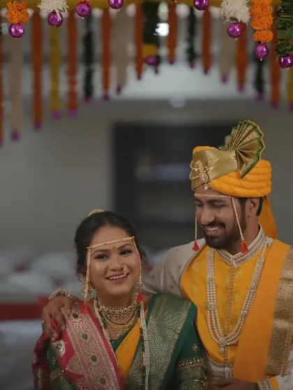 A happy portrait of the newly married couple under a traditional marigold garland canopy, embodying the festive spirit of a Marathi wedding.