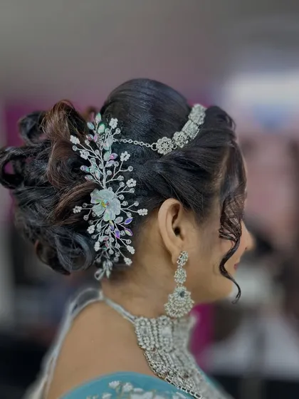 A beautiful messy bun hairstyle for a reception look, adorned with a stunning crystal hairpiece that connects to the 'maang tikka'.