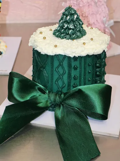 A beautiful green Christmas sweater cake, finished with a large satin bow. It's the perfect centerpiece for a cozy holiday gathering.