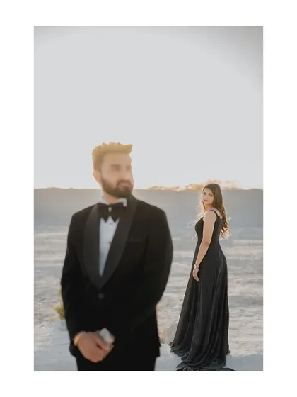 A stylish portrait with a focus on the groom in his sharp tuxedo, while the bride stands elegantly in the background. This composition creates a sense of drama and sophistication.