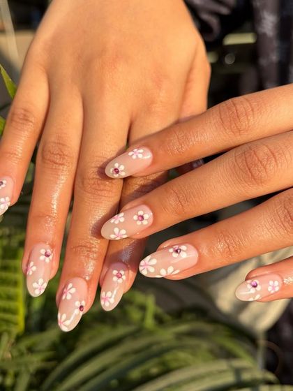 Turn your fingertips into a delicate masterpiece. This nail art features a soft, neutral base with hand-painted white daisies and a single rhinestone accent for a touch of sparkle. It's subtle, elegant, and perfect for spring.