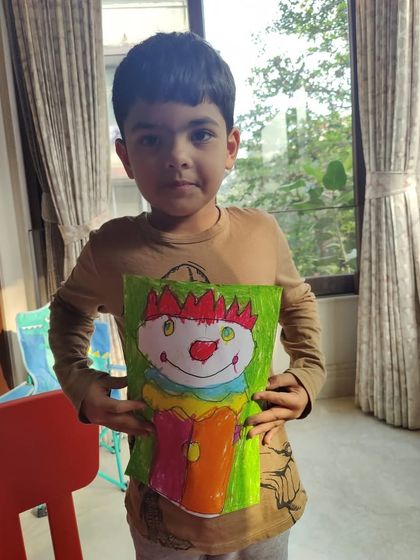 A young student proudly holds up his colorful clown drawing. The smile on his face is the best reward, showing the pride that comes from independent creation.