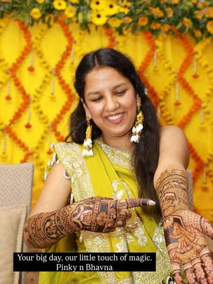 Your big day, our little touch of magic. A happy bride pointing to her intricate mehndi design, filled with personal stories.