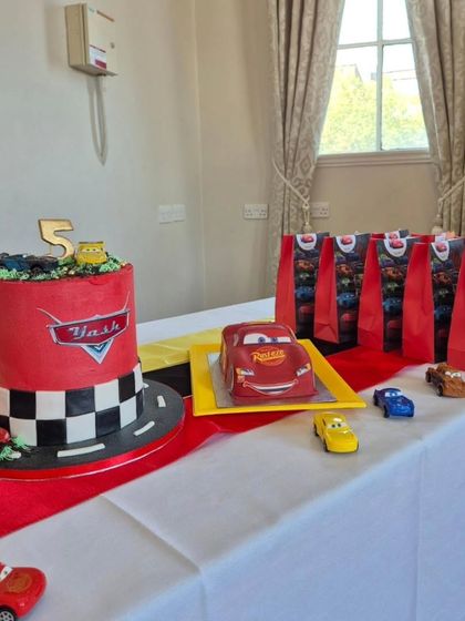A themed dessert table with a Cars cake, cupcakes, and party favor bags.