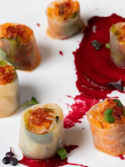 Vietnamese style summer rolls with a vibrant beetroot sauce. The presentation is clean and artistic, highlighting the freshness of the ingredients inside.