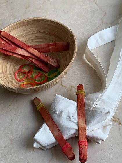 The preparation for a shibori tie-dye workshop. A plain white tote bag is folded and bound with ice cream sticks and rubber bands to resist the dye and create a pattern.