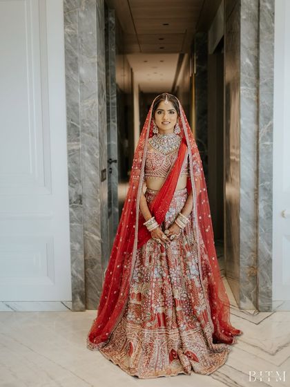 A full-length view of the bride in her magnificent red lehenga. The entire look is a perfect blend of tradition and modern elegance.