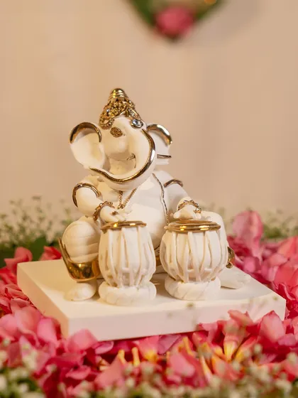A playful and divine depiction of Lord Ganesha with a set of tablas. This white and gold porcelain idol captures his joyful spirit and love for music, making it a delightful addition to your festive decor.