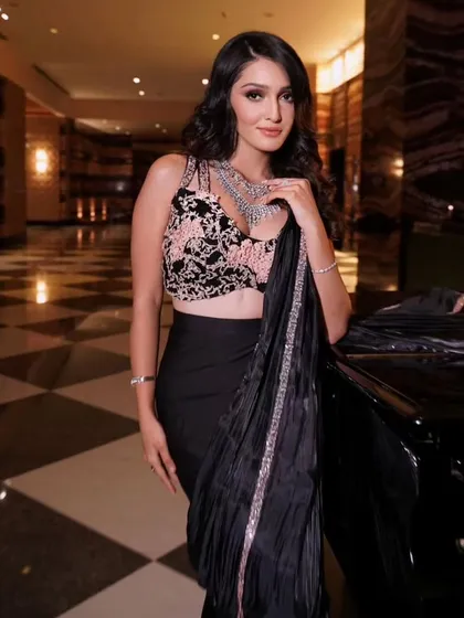 The embroidered blouse contrasts beautifully with the sleek black satin. The drape is designed to highlight the intricate details of the blouse.