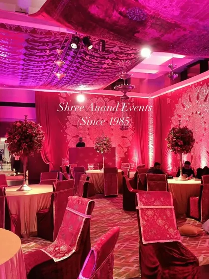 An immersive event space bathed in magenta light, with elegantly set tables and a DJ booth, ready for a night of celebration.