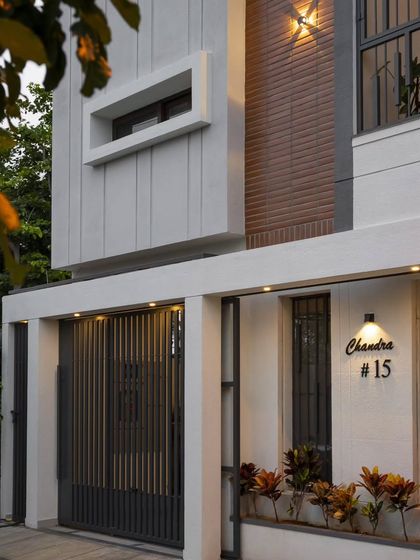 A close-up of the entrance at the Banashankari residence. The custom-designed gate with vertical slats and the integrated planter box soften the frontage, complementing the home's clean color palette and material contrast.