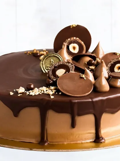 A decadent chocolate drip cake, generously topped with whole hazelnuts, chocolate discs, and praline cones. The rich chocolate frosting and dripping ganache make this a dream for any chocolate aficionado.