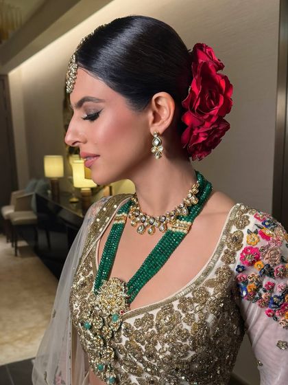 A side profile of the bride, her sleek bun adorned with a large red rose, perfectly complementing her emerald jewelry.