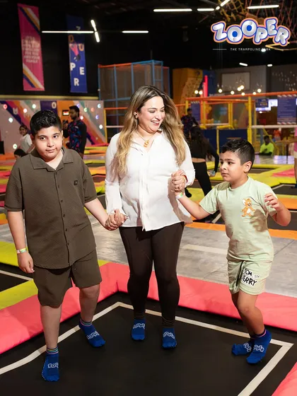 A mother holds hands with her two sons, sharing a moment of family fun on the trampolines.