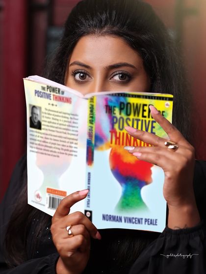 A creative portrait where the model's face is partially obscured by a book. This shot is simple yet intriguing, focusing on the eyes and the theme of positive thinking.
