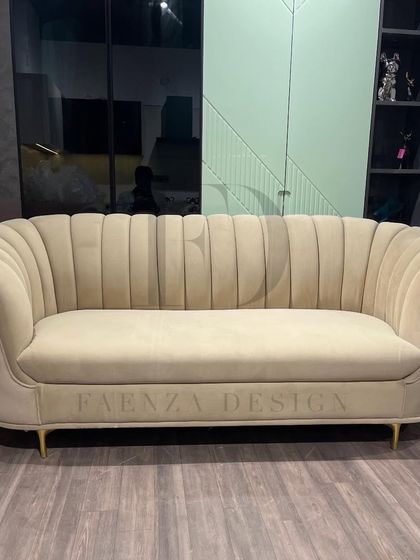 This sofa features a beautiful scalloped, channel-tufted back in a soft beige fabric. The elegant curves and brass-finished legs give it a touch of Art Deco-inspired glamour.
